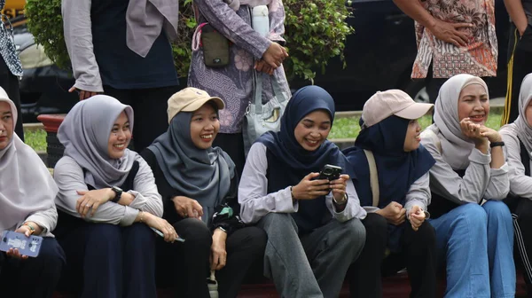 Bir grup insan bankta oturuyor, biri gülüyor. Sahne neşeli ve dost canlısı, Pekalongan Endonezya, 14 Ağustos 2025