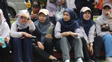 Bir grup insan bankta oturuyor, biri gülüyor. Sahne neşeli ve dost canlısı, Pekalongan Endonezya, 14 Ağustos 2025