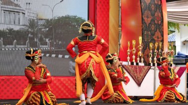 Canlı kırmızı ve altın kostümlü geleneksel dansçılar sahnede zarif bir performans sergilerler, arkalarında ödüller, bayramlık bir etkinlikte kültürel mirası kutlarlar, Pekalongan Endonezya, 6 Kasım 2025