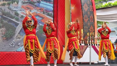 Canlı kırmızı ve altın kostümlü geleneksel dansçılar sahnede zarif bir performans sergilerler, arkalarında ödüller, bayramlık bir etkinlikte kültürel mirası kutlarlar, Pekalongan Endonezya, 6 Kasım 2025