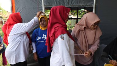 Topluluk üyeleri ücretsiz sağlık tarama programına katılırken, sağlık personeli vücut büyüklüğünü ölçüyor ve yerel bir etkinlik olan Pekalongan, Endonezya 'da temel sağlık hizmetlerini sunuyor, 29 Ağustos 2025