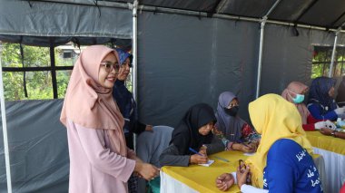 Topluluk üyeleri ücretsiz sağlık tarama programına katılırken, sağlık personeli vücut büyüklüğünü ölçüyor ve yerel bir etkinlik olan Pekalongan, Endonezya 'da temel sağlık hizmetlerini sunuyor, 29 Ağustos 2025