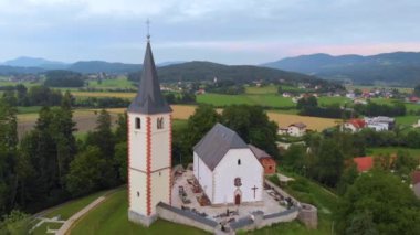 Slovenya 'nın Orta Avrupa köyündeki bir kilisenin manzara manzaralı, ev ve dağların arka planda yer aldığı hava görüntüleri