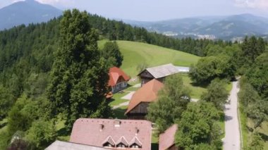 Slovenya 'nın çayırları ve ormanlarıyla çevrili dağlık bir bölgenin tepesindeki uzak bir çiftlik köyünün alçak açılı çember görüntüsü.