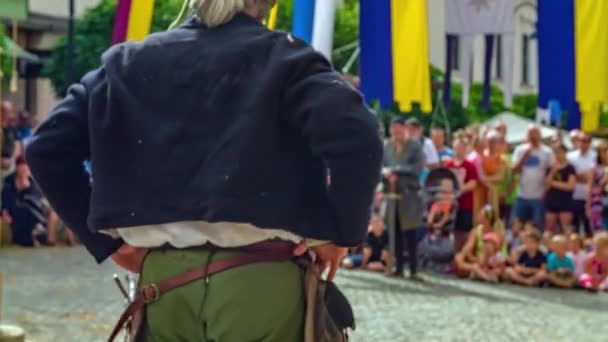 欧洲中世纪的一个节日 一个穿着旧衣服 腰带上挂着剑的男人 在广场上向众人讲述着他的故事 在后台观看演出的人群 纵向拉皮条 — 图库视频影像