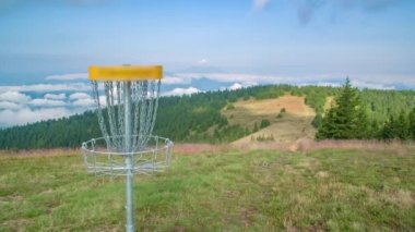 Disk golf hedefi veya sepeti açık bir doğal parktaki bir disk tarafından fırlatılır.