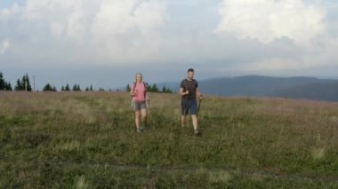 Maceracı bir sırt çantalı çift sabahın erken saatlerinde arka planda büyüleyici manzarayla güzel yeşil dağlara tırmanıyor / geziyor. İnsansız hava aracı görüntüleri.