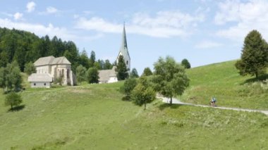 Slovenya 'nın Prevalje kentindeki küçük bir şapele doğru giden bir kır yolunda bisiklet süren iki kişinin havası.