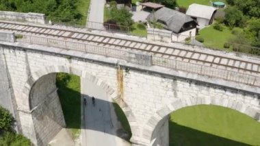 Slovenya 'nın Ravne na koroskem kentindeki bir demiryolu köprüsünün altından geçen iki bisikletçinin hava görüntüsü.