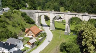İki bisikletçi Slovenya 'da kemerli demiryolu köprüsüne doğru güzel bir kır yolunda bisiklet sürüyor.