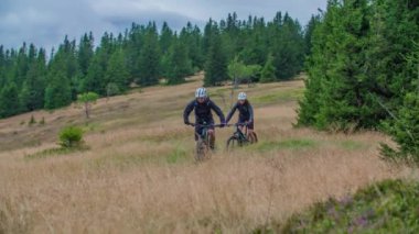 Muhteşem bir tepede giden iki MTB motorcusunu yavaş çekimde. İzleme görüntüsü