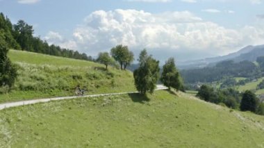 Prevalje Slovenya 'da doğada bir dağ yolu üzerinde bisiklet süren iki kişinin havası, yan izleme çekimi
