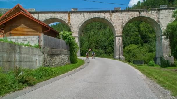 Ciclistas Pareja Ciclismo Bajo Arco Puente Piedra Hacia Cámara — Vídeos de Stock