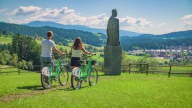 Slovenya 'daki bir köye bakan Lovro Kuhar' ın heykelinin önünden bisikletleriyle geçen genç çift.