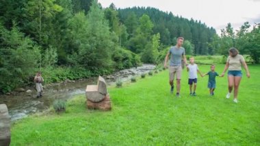 Slovenya 'nın su deresi yakınlarındaki parkta çimlerde yürüyen mutlu bir aile.