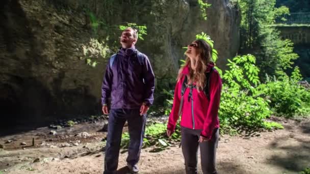 若い魅力的なカップルは大きな洞窟を通って走る蒸気でハイキングを楽しむ — ストック動画