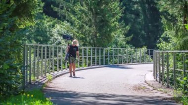 Güzel sarışın kadın doğanın ortasında fotoğraf malzemeleri taşıyor.