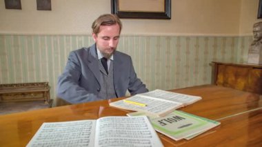 Formaliteler içinde beyaz bir beyefendi, önünde müzik notalarıyla piyano çalıyor. Ön manzara. Yavaş çekim.