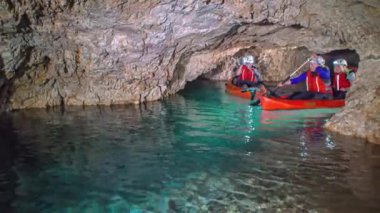 Bir grup turist, karanlık bir mağarada güvenlik teçhizatlarıyla dolaşıyorlar..