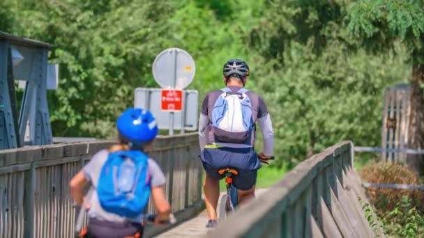 森につながる木製の歩道橋を渡って家族のサイクリングのスローモーション — ストック動画