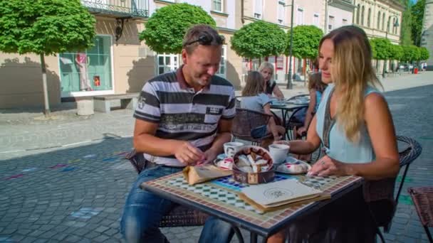 在阳光明媚的日子里 这对快乐且面带微笑的夫妇在户外广场喝咖啡 夏季时间和背景下的教堂 — 图库视频影像