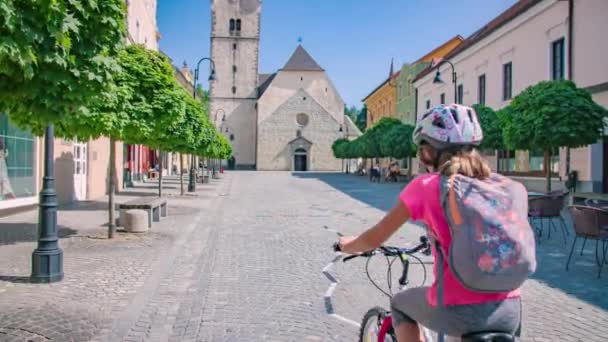 石畳の通り沿いの晴れた日に静かな村を通って教会に4台の自転車に乗る家族 — ストック動画