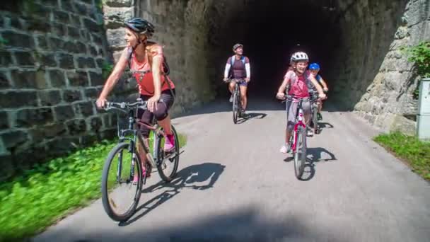 Rodzina Czterech Jeździ Rowerami Wąską Ścieżką Tunelu Natury Ojciec Wskazuje — Wideo stockowe