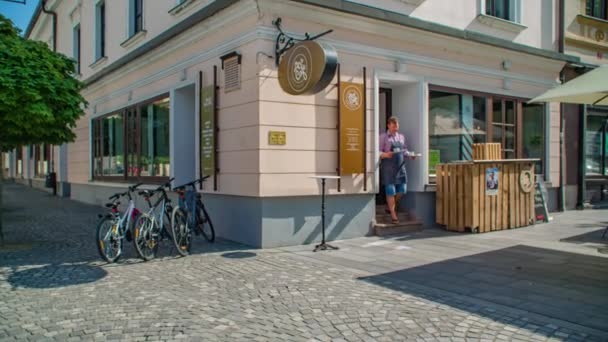 晴れた日にはスロベニアの旧市街広場のカフェでお客様にサービスを提供するウェイター カリンシア 教会を背景に スローモーション — ストック動画