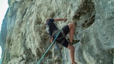 Yakışıklı, güçlü, beyaz bir kaya tırmanışçısı dikey bir uçuruma tırmanıyor. Adrenalin patlaması