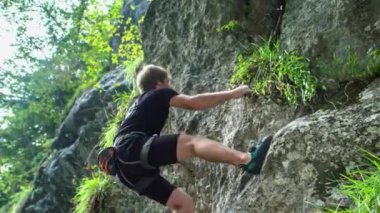 Genç maceracı kaya tırmanışçısı, sarp kayalara halatsız tırmanıyor. Macera ve ekstrem spor anlayışı. Aşağıdan görüntüle.