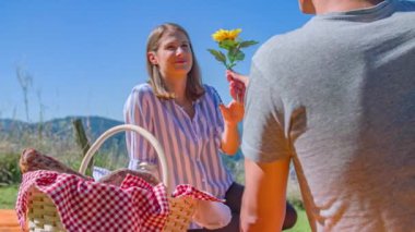 Sevgilisi piknikte sevgilisine romantik bir çiçek sunuyor.