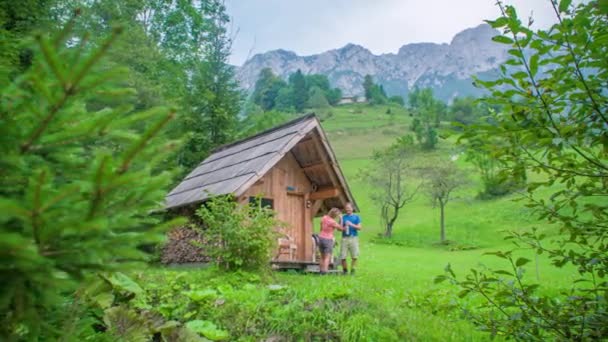 Dospělí Lidé Stojící Dřevěné Chatě Lesa Uprostřed Zeleného Údolí Horami — Stock video