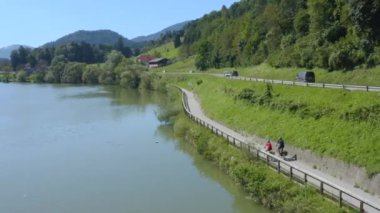 Trafik yolu, geçen arabalar ve nehir kenarında bisiklete binen iki kişi. Hava görüntüleri