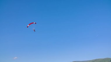 Kırmızı paraşütlü bir paraşütçü çim tarlasına inmeye hazırlanıyor.