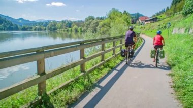 Slovenya, Muta 'da Nehrin Yanındaki Yolda Bisiklet süren çift. Yavaş Hareket, Görüntüyü Takip Et