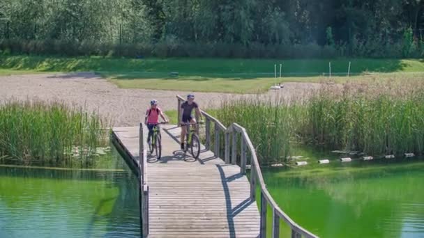 一对男女夫妇在湖边的木桥上骑自行车 — 图库视频影像
