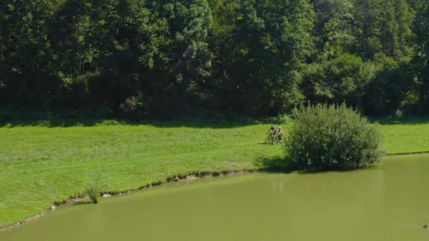 Casal Masculino Feminino Andar Bicicleta Torno Lago Com Casas Atrás — Vídeo de Stock