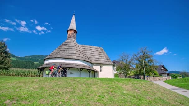 ユニークなロマネスク様式の教会セント ジョン バプテスト教会を通り過ぎるカップルのサイクリスト — ストック動画