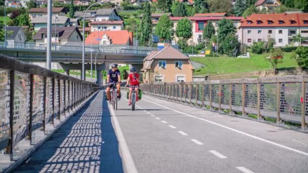 Χαμογελαστό Ζευγάρι Ποδηλασία Πάνω Από Μια Γέφυρα Και Κυματίζει Slovenj — Αρχείο Βίντεο