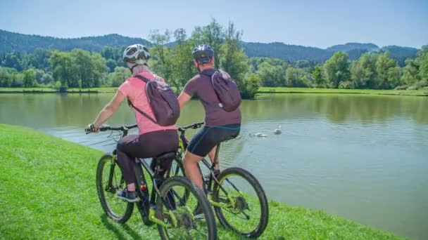 Paar Maakt Een Fietstocht Een Grazige Oever Van Een Meertje — Stockvideo