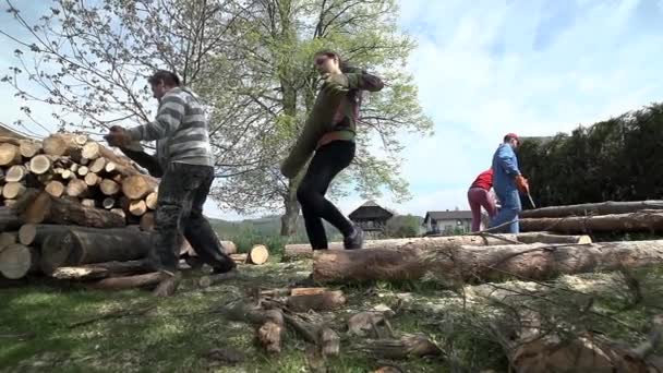 Hembra y hombre llevando grandes troncos a la pila de madera — Vídeo de stock