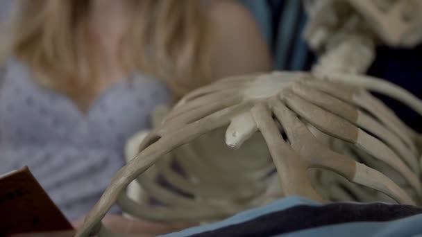 Женщина лежит со скелетом и читает — стоковое видео