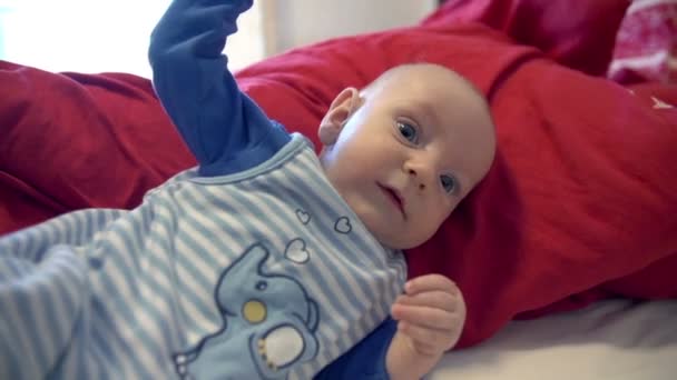 Baby liegt auf roter Bettdecke und winkt — Stockvideo