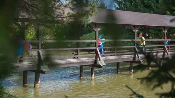 Children running over the wooden bridge over the river — Stock Video