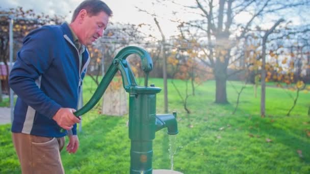 Человек откачивает воду из винтажного водяного насоса — стоковое видео