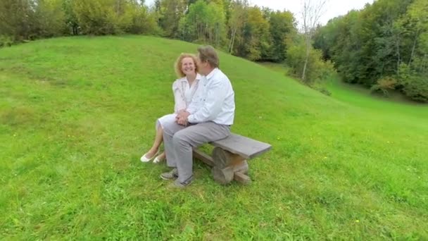 Пара сидит на скамейке и улыбается друг другу — стоковое видео