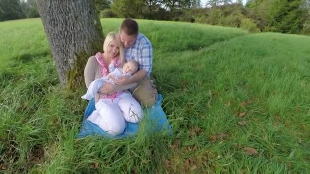 Familia en un campo de hierba bajo un árbol — Vídeos de Stock