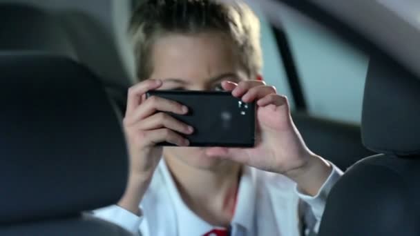 Niño jugando con un teléfono en el asiento trasero — Vídeos de Stock