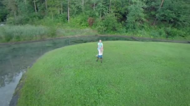 Мальчик и девочка кружатся на траве с водой вокруг — стоковое видео