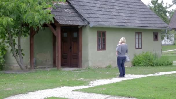 Mãe com bebê andando entre as casas da aldeia — Vídeo de Stock